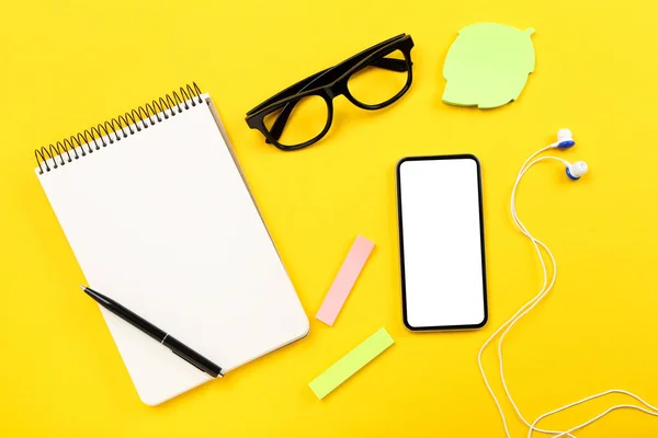 Smartphone mit Kopfhörer, Brille und Notizblock auf gelbem Backgro — Stockfoto