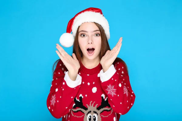美しい女性でクリスマスセーターとサンタ帽子上の青の背景 — ストック写真