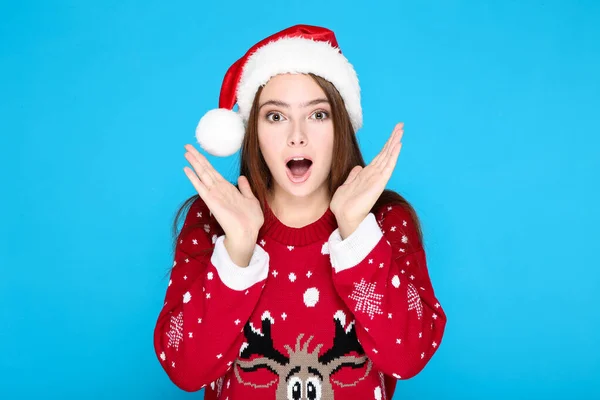 Mulher bonita em camisola de Natal e chapéu de santa no fundo azul — Fotografia de Stock