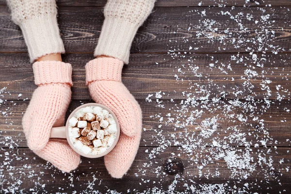 Hands in knitted mittens holding cup of hot drink on wooden tabl — Stock Photo, Image