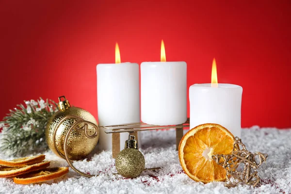 Рождественские свечи с безделушками, сухими апельсинами и санями на красной бабе — стоковое фото