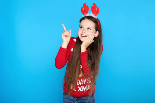 Κοριτσάκι με χριστουγεννιάτικο πουλόβερ και κόκκινα κέρατα που δείχνουν με πτερύγιο — Φωτογραφία Αρχείου