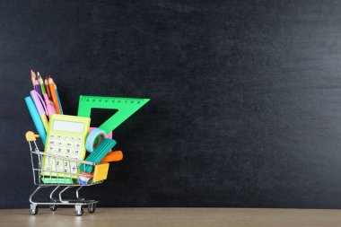 Okul malzemeleri karatahta arka planda alışveriş arabasında.