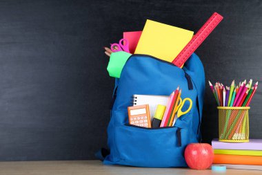 Kara tahta arka planda mavi sırt çantası ile okul malzemeleri
