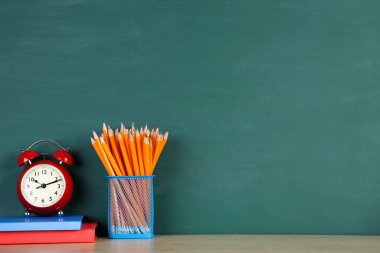 Yeşil arka planda kırmızı alarmlı okul malzemeleri.