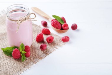 Cam kavanozda ahududu püresi ve beyaz ahşap masa üzerinde kaşık.