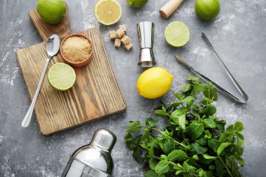 Gri ahşap masada limonlu, limonlu ve nane yapraklı barmen ekipmanları.