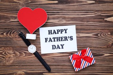Mutlu Babalar Günü 'nü kırmızı kalple, hediye kutusuyla ve tahta masada kol saatiyle yaz.
