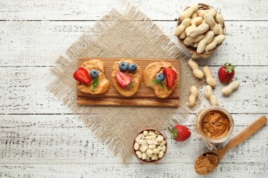 Beyaz ahşap masada fıstık ezmesi, meyve ve fındık ile Ekmek