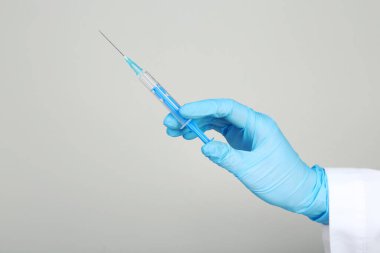 Eldivenli doktor gri arka planda şırınga tutuyor.