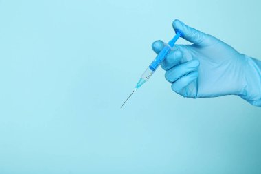 Eldivenli doktor mavi arka planda şırınga tutuyor.
