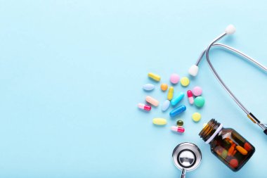 Şişeli ilaç hapları ve mavi arka planda steteskop.