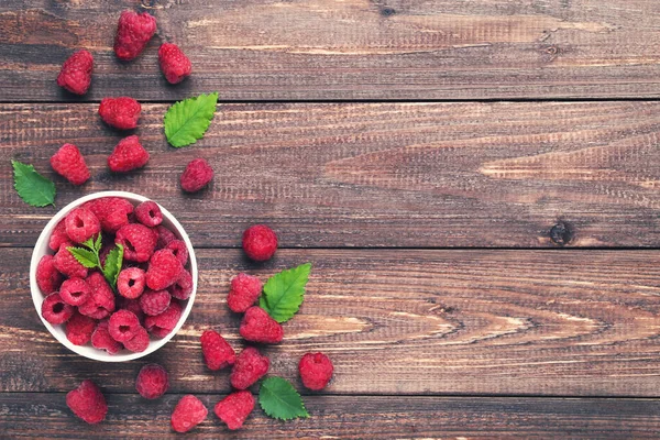 Sweet raspberries with green leafs in bowl on brown wooden table