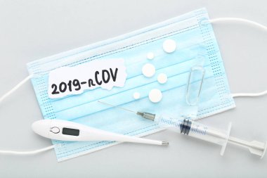Termometresi, hapları, şırıngası ve gri arkaplanı olan metin 2019-nCov