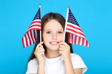 Mavi arka planda Amerikan bayrakları tutan genç kız.