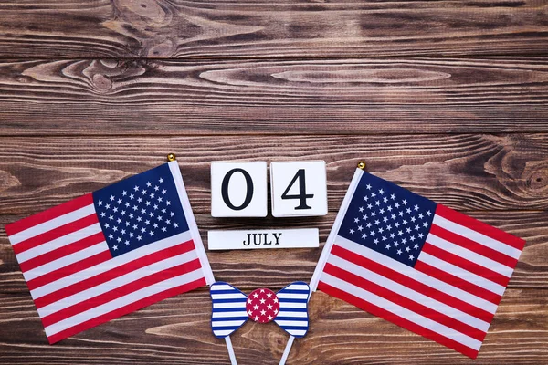 Independence Day concept. American flags with paper bow tie and cube calendar on wooden table