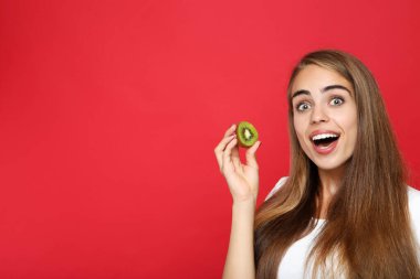 Kırmızı arka planda kivi meyvesi tutan genç kız.