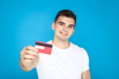 Genç adam mavi arka planda kredi kartı gösteriyor.