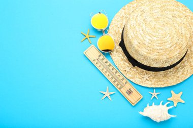 Güneş gözlüklü, termometresi ve mavi arka planda deniz kabukları olan yaz hasır şapkası.