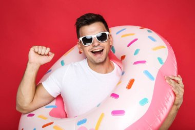 Kırmızı arka planda şişme donutu olan genç bir adam.