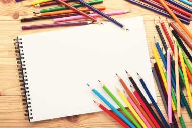 Kahverengi ahşap masa üzerinde defter olan renkli kalemler.