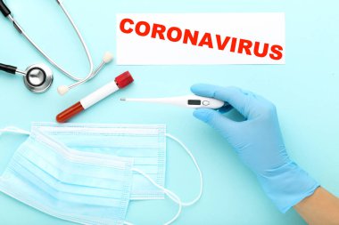 Doktor termometreyi ilaç maskesi, test tüpü ve mavi arkaplan üzerine yazı ile tutuyor.