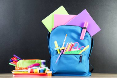 Siyah arka planda okul malzemeleriyle dolu sırt çantası.