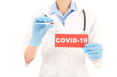 Doktor termometreyi ve kağıdı Covid-19 metniyle tutuyor
