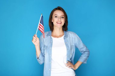 Güzel genç bir kadın mavi arka planda Amerikan bayrağını tutuyor.