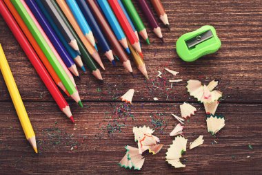 Kahverengi ahşap masada talaşlı renkli kalemler ve keskinleştirici.