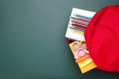 Yeşil arka planda okul malzemeleriyle dolu sırt çantası.