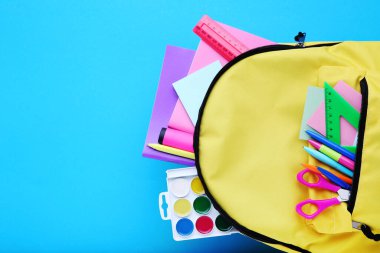 Mavi arka planda okul malzemeleri olan sırt çantası.