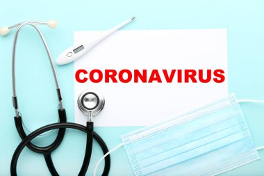 Mavi zemin üzerinde termometre, steteskop ve ilaç maskesi olan Coronavirus 'u metin