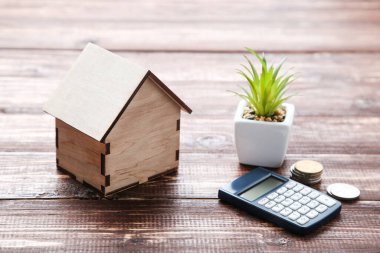 Kahverengi ahşap masada madeni paralar ve hesap makineli ev modeli