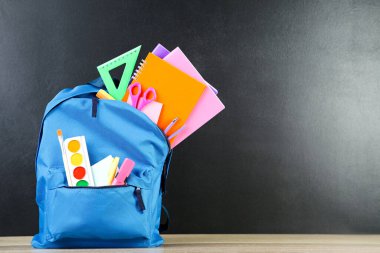 Siyah arka planda okul malzemeleriyle dolu sırt çantası.
