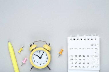 Gri zemin üzerinde alarm saati ve kalem bulunan takvim sayfası