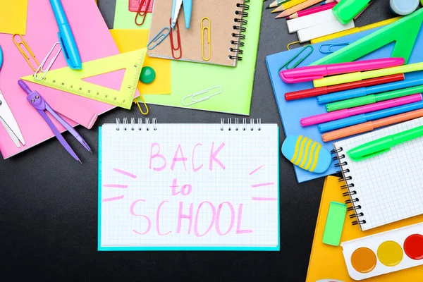 Farklı okul malzemeleri ve siyah arka planda okula dönüş metni.