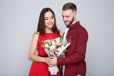 Gri arka planda bir buket çiçekli mutlu genç çift