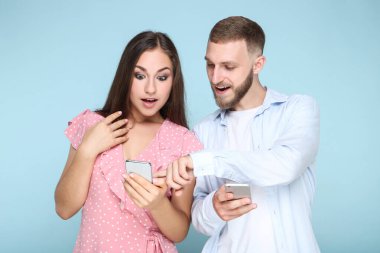 Mavi arka planda cep telefonları olan mutlu genç çift.