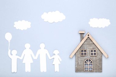 Gri arka planda bulutlu ve evi olan kağıt aile figürleri