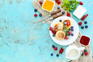 Tatlı peynirli krep, böğürtlenli kase, krema ve reçel mavi arka planda.