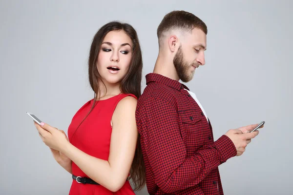 Happy young couple with mobile phones on grey background