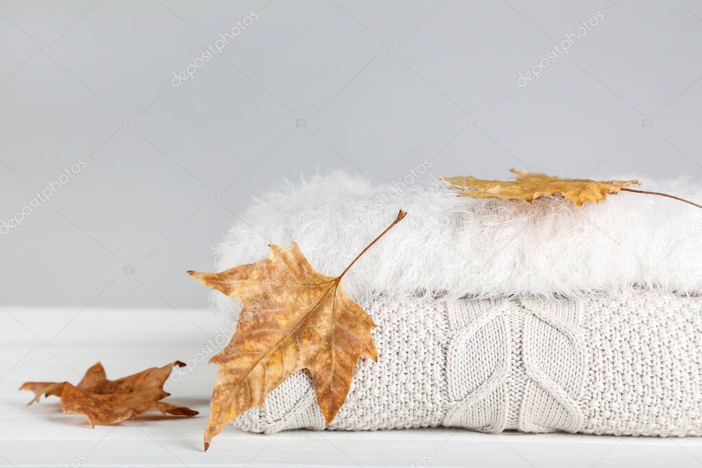 Folded sweaters with autumn leafs on grey background