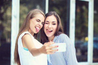 Dillerini gösteren ve cep telefonuyla selfie çeken iki genç kız arkadaş.