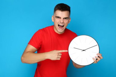 Mavi arka planda saati olan genç adam.