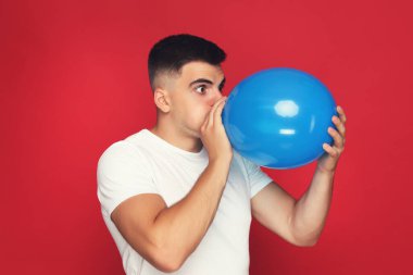 Kırmızı arka planda balon şişiren Yuong adamı.