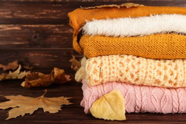 Kahverengi ahşap masada sonbahar yapraklı katlanmış süveterler.