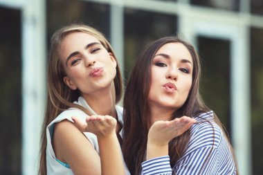 İki genç mutlu kız arkadaş havada öpüşüyor.