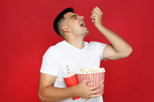 Junger Mann Mit Eimer Popcorn Und Pappbecher Auf Rotem Hintergrund — Stockfoto