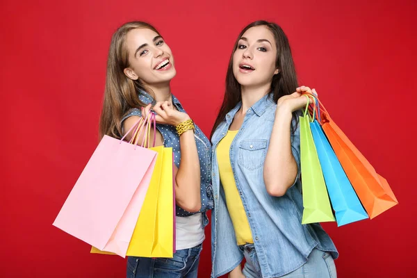 Junge Glückliche Freundinnen Mit Einkaufstaschen Auf Rotem Hintergrund — Stockfoto